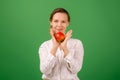 A pretty woman of middle age in a white shirt holds an apple in her hand on a green background. Healthy eating, vegetarianism, Royalty Free Stock Photo