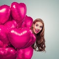 Pretty woman peeks out from pink heart balloons and laughing
