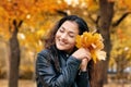 Pretty woman is posing with bunch of maple`s leaves in autumn park. She`s closing eyes and dreaming. Beautiful landscape at fall Royalty Free Stock Photo