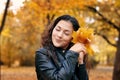 Pretty woman is posing with bunch of maple`s leaves in autumn park. She`s closing eyes and dreaming. Beautiful landscape at fall Royalty Free Stock Photo