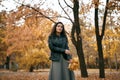 Pretty woman posing with maple`s leaf in autumn park near big tree. Beautiful landscape at fall season Royalty Free Stock Photo