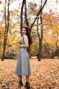 Pretty woman posing with maple`s leaf in autumn park near big tree. Beautiful landscape at fall season Royalty Free Stock Photo