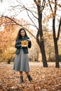 Pretty woman posing with maple`s leaf in autumn park near big tree. Beautiful landscape at fall season Royalty Free Stock Photo