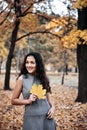 Pretty woman posing with maple`s leaf in autumn park near big tree. Beautiful landscape at fall season Royalty Free Stock Photo