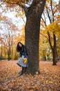 Pretty woman posing with maple`s leaves in autumn park near big tree. Beautiful landscape at fall season Royalty Free Stock Photo