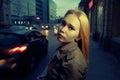 Pretty woman posing in pensive state of mind in the night street with blurred cars and streetlights on background, toned