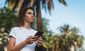 Pretty woman reads text message on mobile smartphone while standing in a Park on a warm summer day, gorgeous woman listens to mus