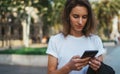 Pretty woman reads text message on mobile smartphone while standing in a Park on warm summer day, gorgeous woman listens