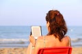 Pretty woman on red chair reads the ebook on the beach in summer Royalty Free Stock Photo