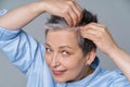 Pretty woman in 50s checking her hair or skull skin in mirror. Beautiful grey haired woman dealing with dandruff problem Royalty Free Stock Photo