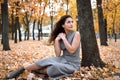 Pretty woman is sitting in autumn park near big tree. Beautiful landscape at fall season Royalty Free Stock Photo