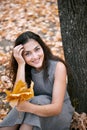 Pretty woman is sitting in autumn park near big tree. Beautiful landscape at fall season Royalty Free Stock Photo