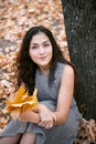 Pretty woman is sitting in autumn park near big tree. Beautiful landscape at fall season Royalty Free Stock Photo