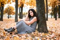 Pretty woman is sitting in autumn park near big tree. Beautiful landscape at fall season Royalty Free Stock Photo