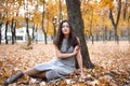 Pretty woman is sitting in autumn park near big tree. Beautiful landscape at fall season Royalty Free Stock Photo