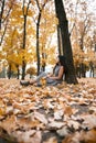Pretty woman is sitting in autumn park near big tree. Beautiful landscape at fall season Royalty Free Stock Photo