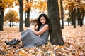 Pretty woman is sitting in autumn park near big tree. Beautiful landscape at fall season Royalty Free Stock Photo