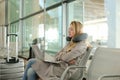 Pretty woman sitting in waiting room with laptop near valise, using neck pillow. Royalty Free Stock Photo