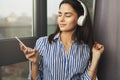 Pretty woman sitting by window and listening to relaxing music in headphones. Stream favorite songs directly from social networks Royalty Free Stock Photo