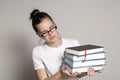 Pretty woman student with glasses holds a stack of heavy books in hands and looks at them puzzled Royalty Free Stock Photo