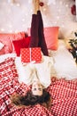 Pretty woman in sweater lies on the sofa with present gift for christmase, shiny christmas tree, garlands and balls, new Royalty Free Stock Photo