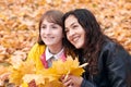 Pretty woman and teen girl are posing with bunch of maple`s leaves in autumn park. Beautiful landscape at fall season Royalty Free Stock Photo