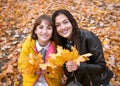 Pretty woman and teen girl are posing with bunch of maple`s leaves in autumn park. Beautiful landscape at fall season Royalty Free Stock Photo