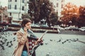 Pretty woman tourist talking on mobile phone while looking at map of the city, surrounded by flying pigeons on a square. Royalty Free Stock Photo