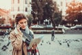 Pretty woman tourist talking on mobile phone while looking at map of the city, surrounded by flying pigeons on a square. Royalty Free Stock Photo
