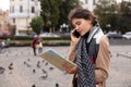 Pretty woman tourist talking on mobile phone while looking at map of the city, surrounded by flying pigeons on a square. Royalty Free Stock Photo