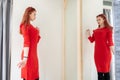 Pretty woman trying on clothes in a fitting shop. the lady in the red dress is reflected in the mirror Royalty Free Stock Photo