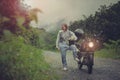 pretty woman wearing plastic rain clothes holding safety helmet standing beside small enduro motorcycle