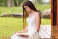 Pretty woman in white dress reading book in the cloudy nature. Girl sits on the terrace or on the porch Royalty Free Stock Photo