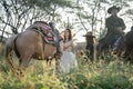 Pretty woman with white dress stand near horse and Asian man with cowboy costume stay on horse that look like he guard or protect Royalty Free Stock Photo