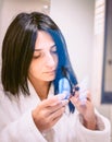 Pretty Woman in white robe suspiciously touching her hair ends in bathroom Royalty Free Stock Photo