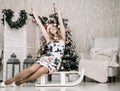 Pretty woman in white tight dress and red santa hat indoors near decorated fir tree alone Royalty Free Stock Photo