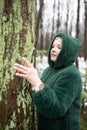 Pretty woman in winter forest. Female portrait in snow park. Woman in hood of eco fur jacket touch with hand tree trunk. Royalty Free Stock Photo