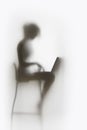 Pretty woman works on laptop computer behind a diffuse white curtain. Body silhouette of a typing lady.