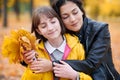 Pretty woman and teen girl are posing with bunch of maple`s leaves in autumn park. They are closing eyes and dreaming. Beautiful Royalty Free Stock Photo