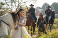 Pretty woman with white dress stand near horse and Asian man with cowboy costume stay on horse that look like he guard or protect Royalty Free Stock Photo