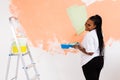 Pretty young african american woman with painting roller indoors. Redecoration, renovation, apartment repair and Royalty Free Stock Photo