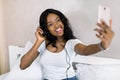 Pretty young African American woman relaxing, listening to music using earphones and smartphone, making selfie photo Royalty Free Stock Photo