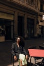 Pretty young african woman sitting in cafe on terrace relaing and enjoying sunny weather.