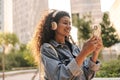 Pretty young african woman is using smartphone, laptop standing outdoors. Royalty Free Stock Photo