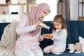 Pretty young Arabian mother in beige headscarf, ready to apply skin cream or lotion on her little daughter hands Royalty Free Stock Photo