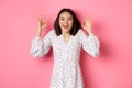 Pretty young asian woman in dress showing okay sign, praising and showing approval, looking satisfied, standing against Royalty Free Stock Photo