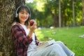 Pretty young asian woman eating apple under huge tree on green grass at sunny beautiful garden background Royalty Free Stock Photo