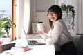 Pretty young asian woman employee holding paper cup, sitting at her office desk and smiling to camera Royalty Free Stock Photo