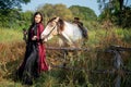 Pretty young Asian woman stand and lay to fence near white horse also look at camera in field Royalty Free Stock Photo