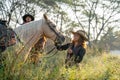 Pretty young Asian woman with cowboy costume smile and stand in front of white horse and stay near other cowboy man in field near Royalty Free Stock Photo